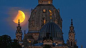 Der Mond geht am Morgen während einer partiellen Mondfinsternis hinter der Frauenkirche und der Kuppel der Kunstakedmie mit dem Engel ...