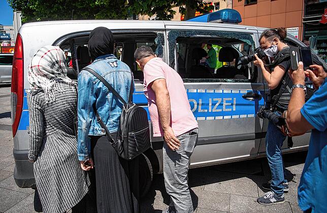 Passanten und ein Pressefotograf betrachten ein während der nächtlichen Randale in Stuttgart beschädigtes Polizeiauto.