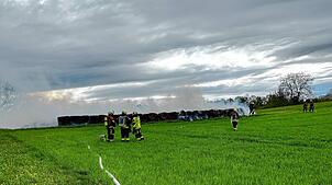 Einsatzkräfte mit Atemschutzmasken löschen am Sonntag, 20. April, die brennenden Strohballen.