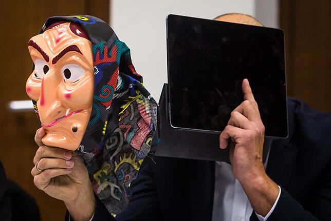 Ein Angeklagter sitzt während der Verhandlung in einem Raum des Amtsgerichts Heilbronn auf seinem Platz und hält eine Hexenmaske in ...