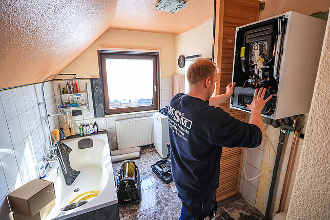 Ein Mitarbeiter einer Sanitär- und Heizungsbaufirma installiert eine moderne Gasbrennwerttherme in einem Einfamilienhaus. Im Moment ...