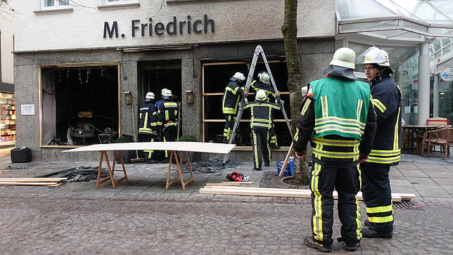 Einsatzkräfte der Feuerwehr sichern am Vormittag das vollkommen zerstörte Geschäft in der Fußgängerzone.