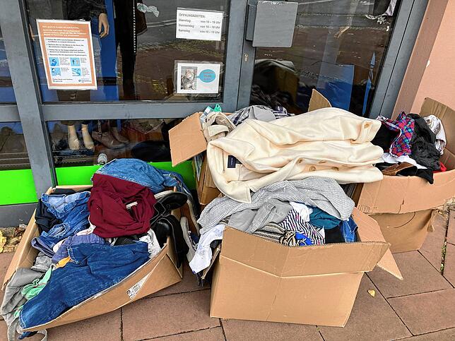 Einfach direkt vor die Tür des Kleiderladens gestellt: mehrere offene Kartons mit Bekleidung. Die meisten Jacken, Blusen und Hemden, ...