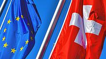 Die Nationalflagge der Schweiz (r) weht neben der Flagge der EU vor blauem Himmel.
