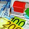 Ein Spielzeughaus und die Nachbildung von Euro-Geldscheinen liegen auf einem Abgabenbescheid für die Entrichtung der Grundsteuer.
