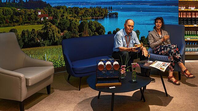 Jürgen und Sabine Goldmann in der Lounge vor einer Fototapete, die neben einer Verkostungstheke mit regionalen Produkten für ein ...