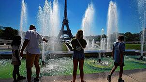 Touristen stehen an den Springbrunnen der Grünanlage Jardins du Trocadero neben dem Eiffelturm, während ganz Europa gerade von starker ...
