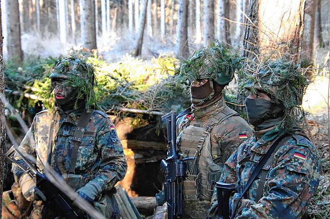 Helme und Gesichter getarnt: Die Jäger-Rekruten werden von ihren Ausbildern in die Lage des Schützengrabens im Wald eingewiesen.