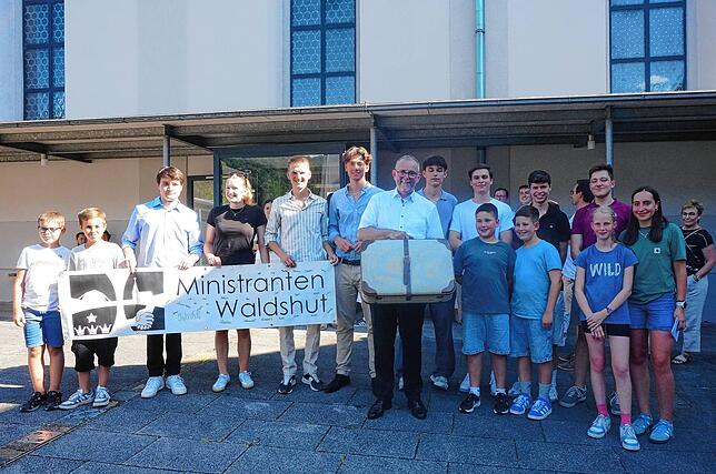 Pfarrer Ulrich Sickinger nach dem Abschiedsgottesdienst auf dem Kirchplatz mit Ministranten, die ihm einen ganzen Koffer voll Geschenke ...