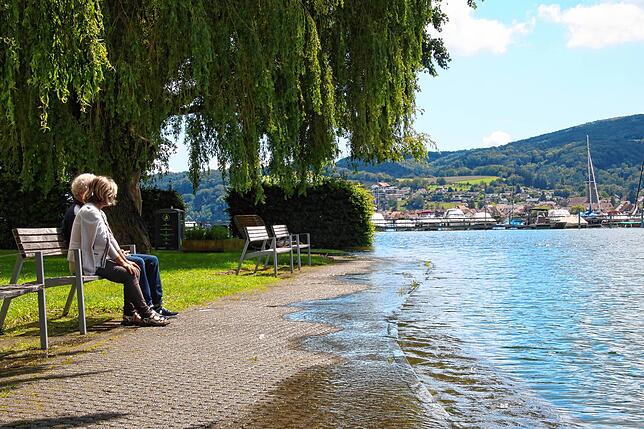 Zwei Personen sitzen auf einer Bank in Gaienhofen, während das Wasser über den Seeweg schwappt.