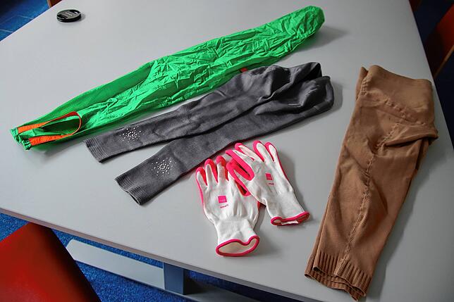 Um ihre Kompressionsstrümpfe (grau: Arme, braun: Beine) anzuziehen, nimmt Rebecca Schuler Handschuhe und einen Strumpf (grün) zur Hilfe.