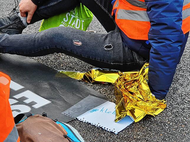 Der Februarasphalt ist kalt: Die angeklebte Hand eines Aktivisten wird mit einer Rettungsdecke gewärmt.