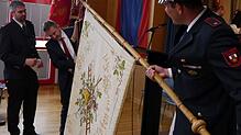 Bürgermeister Jochen Spieß (Mitte) befestigt die Fahnenschleife, die er der Feuerwehrabteilung zu ihrem 125-jährigen Bestehen überreicht ...