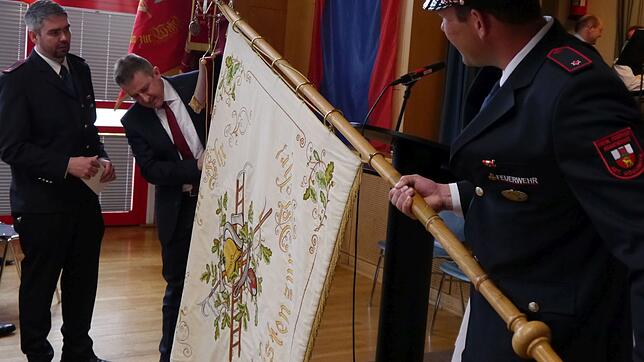 Bürgermeister Jochen Spieß (Mitte) befestigt die Fahnenschleife, die er der Feuerwehrabteilung zu ihrem 125-jährigen Bestehen überreicht ...