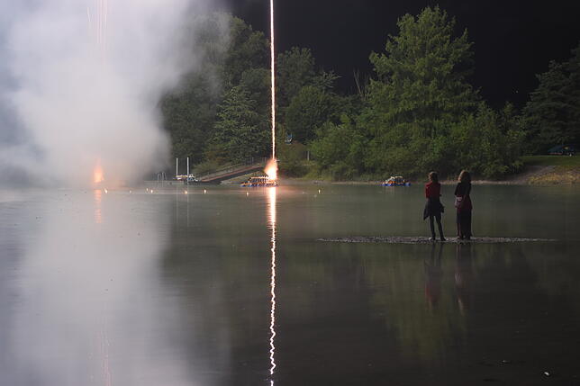 Zweigeteiltes Bild beim Klangfeuerwerk: Das Leuchten einer Rakete im Steigflug, und ihr Spiegelbild im Schlosssee.