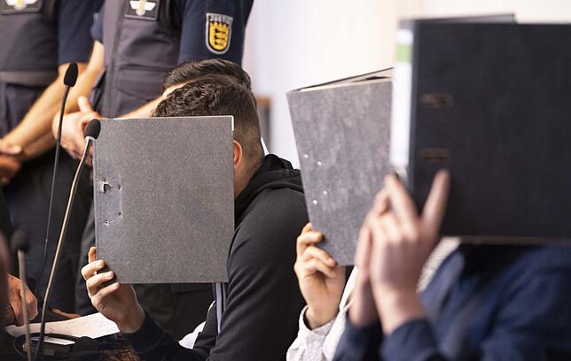 Prozessauftakt im Landgericht Freiburg zur mutmaßlichen Gruppenvergewaltigung: Drei der elf Angeklagten halten Ordner vor ihr Gesicht.