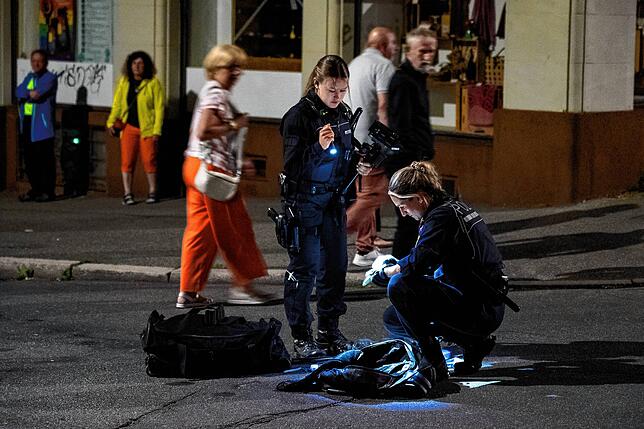 Polizistinnen kontrollieren seine Reisetasche und seinen Rucksack im Licht einer Taschenlampe.