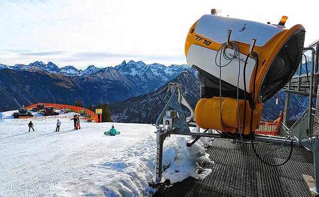 Wintersportler auf dem Fellhorn bei Oberstdorf fahren neben einer Schneekanone den Abhang hinunter. Eine Corona-Wintersport-Konzept wie ...