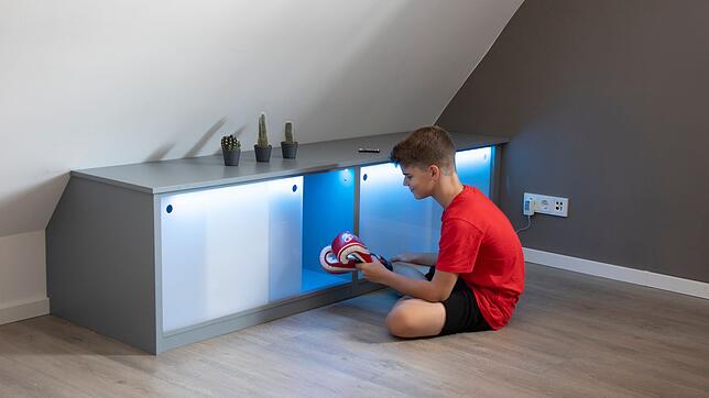 Stauraum unter der Dachschräge: Die Schiebetüren aus Acrylglas werden mit Hilfe eines LED-Bandes von innen indirekt beleuchtet.