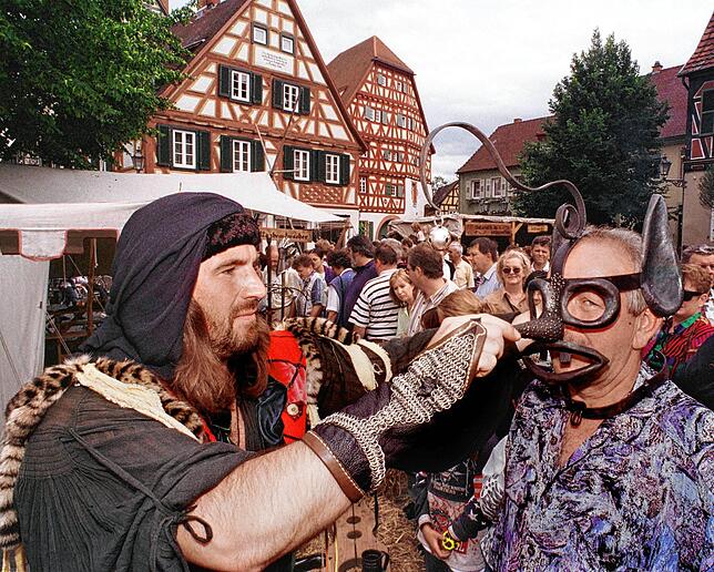 Auf einem Mittelalter-Markt setzt ein Henker (links) einem Mann die Schandmaske auf.