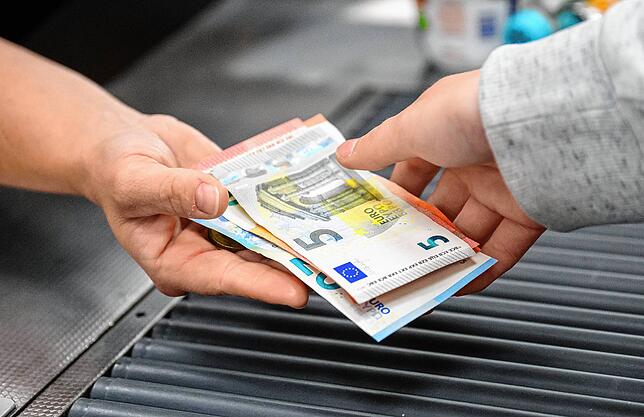 Eine Kassiererin gibt einer Kundin Wechselgeld an der Kasse eines Supermarktes.