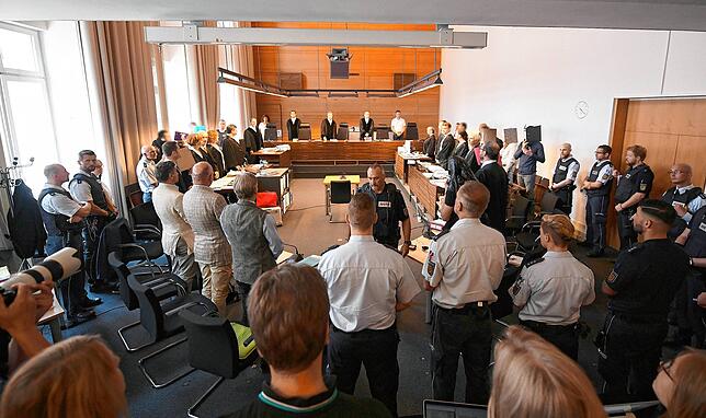 Zu Beginn des Prozesses stehen elf Angeklagte und Justizbeamte im Landgericht seitlich hinter ihren Anwälten. In der Mitte stehen die ...