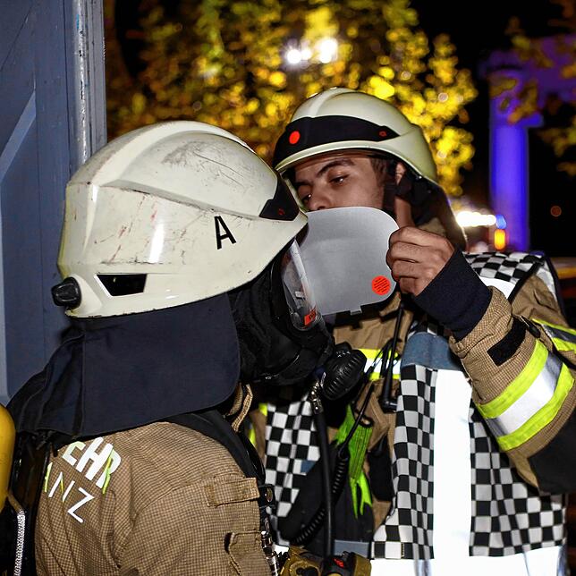 Den Feuerwehrleuten in der Spiegelhalle wird ein Blendschutz auf die Atemschutzmaske aufgeklebt. So soll eine erschwerte Sicht durch ...