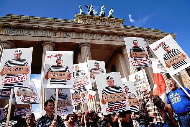 Teilnehmer einer Demonstration gegen die Corona-Maßnahmen halten am Brandenburger Tor Schilder mit Fotos von Politikern, Journalisten ...