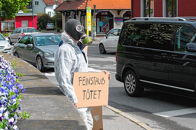 Einer der Aktivisten steht an der Bundesstraße 33, trägt eine Gasmaske und hält eine Papptafel „Feinstaub tötet“.