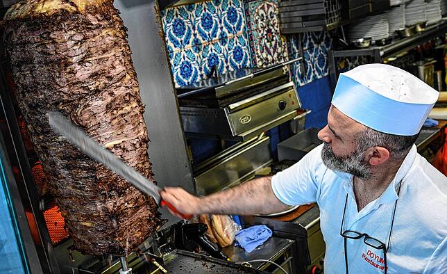 Das Fleisch wird von Dönerverkäufer Suat von einem Dönerspieß mit einem langen Messer geschnitten. Der Spieß ist aus Rindfleisch ...