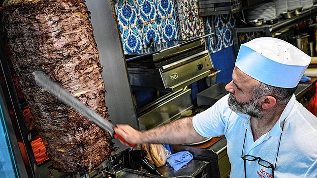 Das Fleisch wird von Dönerverkäufer Suat von einem Dönerspieß mit einem langen Messer geschnitten. Der Spieß ist aus Rindfleisch ...