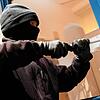 Eine vermummte Person bricht ein Fenster auf (Symbolbild)