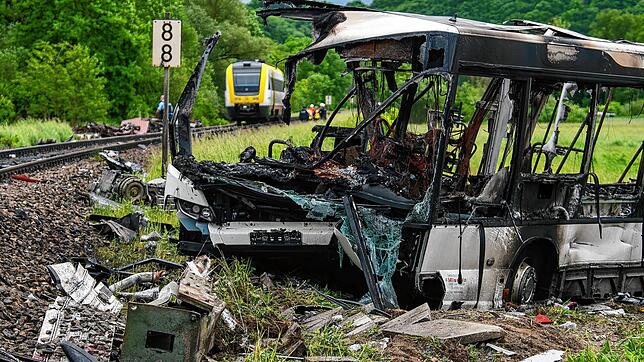 Rettungskräfte stehen an einem ausgebrannten Bus. Dieser Bus kam bei einem Rückstau auf einem Bahnübergang zum Stehen und wurde von ...