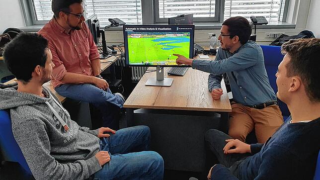 Das Team von Subsequent bei der Analyse eines Fußballspiels, bei dem freie Räume auf dem Bildschirm blau angezeigt werden. Hinten: ...