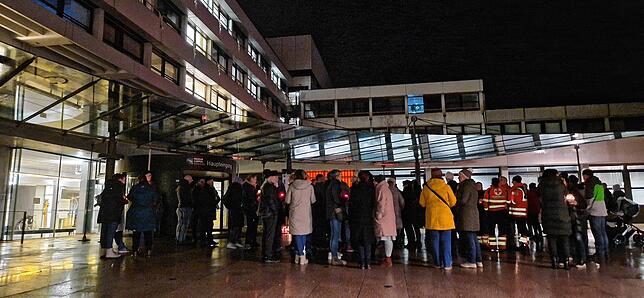 Menschen stehen in kleinen Gruppen auf dem Vorplatz der Klinik.