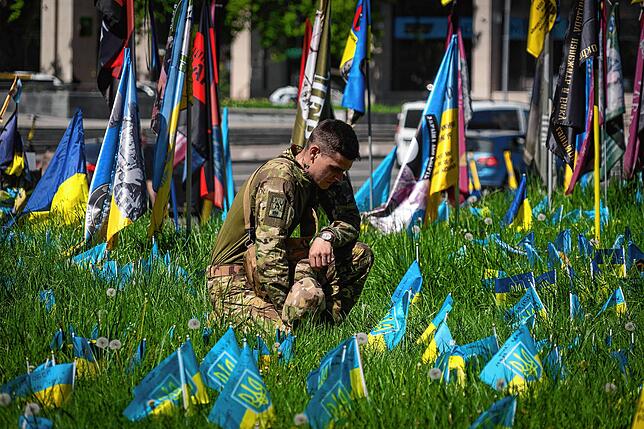 Ein ukrainischer Soldat legt auf dem Unabhängigkeitsplatz in Kiew eine kleine Nationalfahne auf den Rasen, um an einen Kameraden zu ...