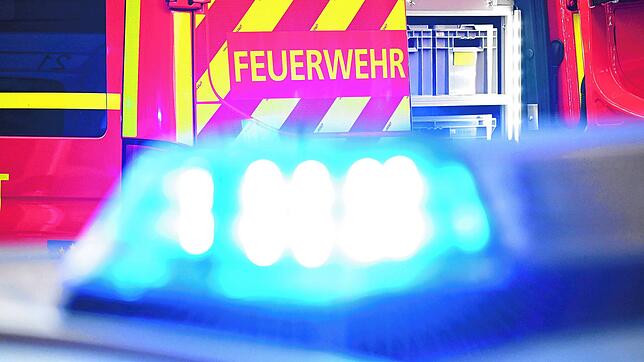 Ein Feuerwehrfahrzeug im Einsatz, davor ein Polizeiauto mit eingeschaltetem Blaulicht (Symbolbild). Ein Schlauchboot mit einem ...