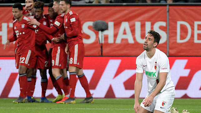 Augsburgs Rani Khedira (r) kniet auf dem Rasen, während die Spieler von München über das 2:3 jubeln.