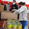 Feuerwehrfrau Gina Steinle packt Lebensmittel in einen Karton für die Ukraine, Hansi Otteny sammelt die Kartons auf einer Palette.