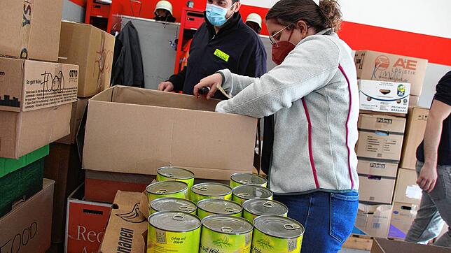 Feuerwehrfrau Gina Steinle packt Lebensmittel in einen Karton für die Ukraine, Hansi Otteny sammelt die Kartons auf einer Palette.