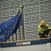Ein Bauarbeiter arbeitet im Außenbereich des Hauptsitzes der EU-Kommission, während neben ihm Europaflaggen wehen.