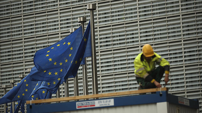 Ein Bauarbeiter arbeitet im Außenbereich des Hauptsitzes der EU-Kommission, während neben ihm Europaflaggen wehen.