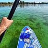 Leuchtend grünes Wasser unter blauem Himmel, von einem SUP-Board aus gesehen. Paddler sollten immer möglichst viel Abstand zu ...