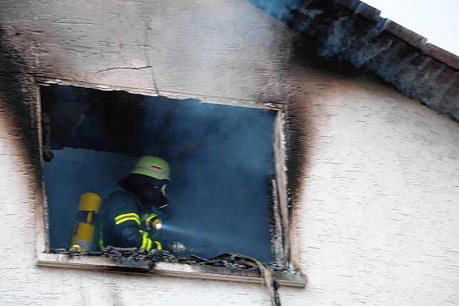 Ein Feuerwehrmann arbeitet nach den Löscharbeiten im Dachgeschoss in unmittelbarer Nähe des Brandherdes.