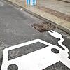 Ein Elektrofahrzeug kennzeichnet einen Parkplatz neben einer Ladesäule an einer Straße.