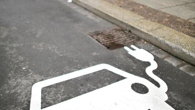 Ein Elektrofahrzeug kennzeichnet einen Parkplatz neben einer Ladesäule an einer Straße.