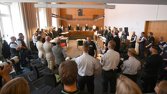 Zu Beginn des Prozesses stehen elf Angeklagte und Justizbeamte im Landgericht seitlich hinter ihren Anwälten. In der Mitte stehen die ...