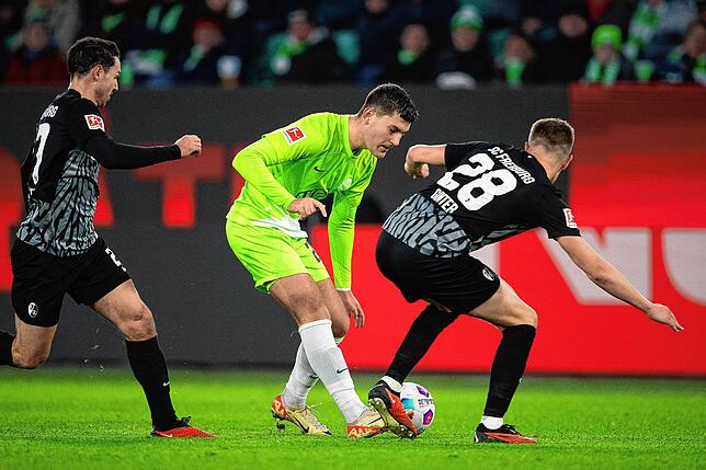 Wolfsburgs Jonas Wind spielt gegen Freiburgs Matthias Ginter (r).