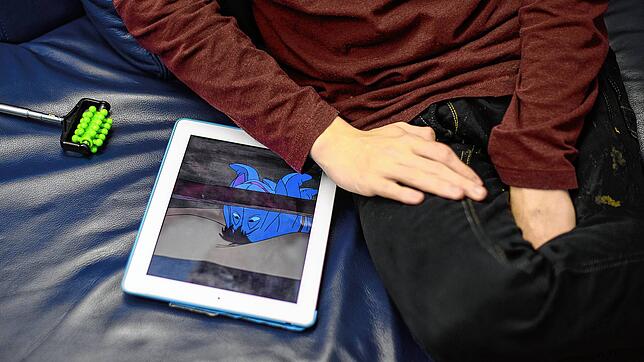 Ein Junge der frühkindlichen Autismus hat, sitzt am neben einem Tablet, auf dem der Esel „I-Aah“ aus der Zeichentrickserie „Pu der Bär“ ...