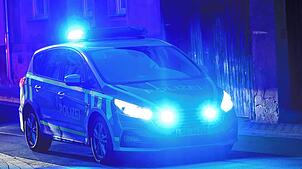 Ein Fahrzeug der Polizei fährt mit Blaulicht am Abend durch eine enge Straße. (Symbolbild)